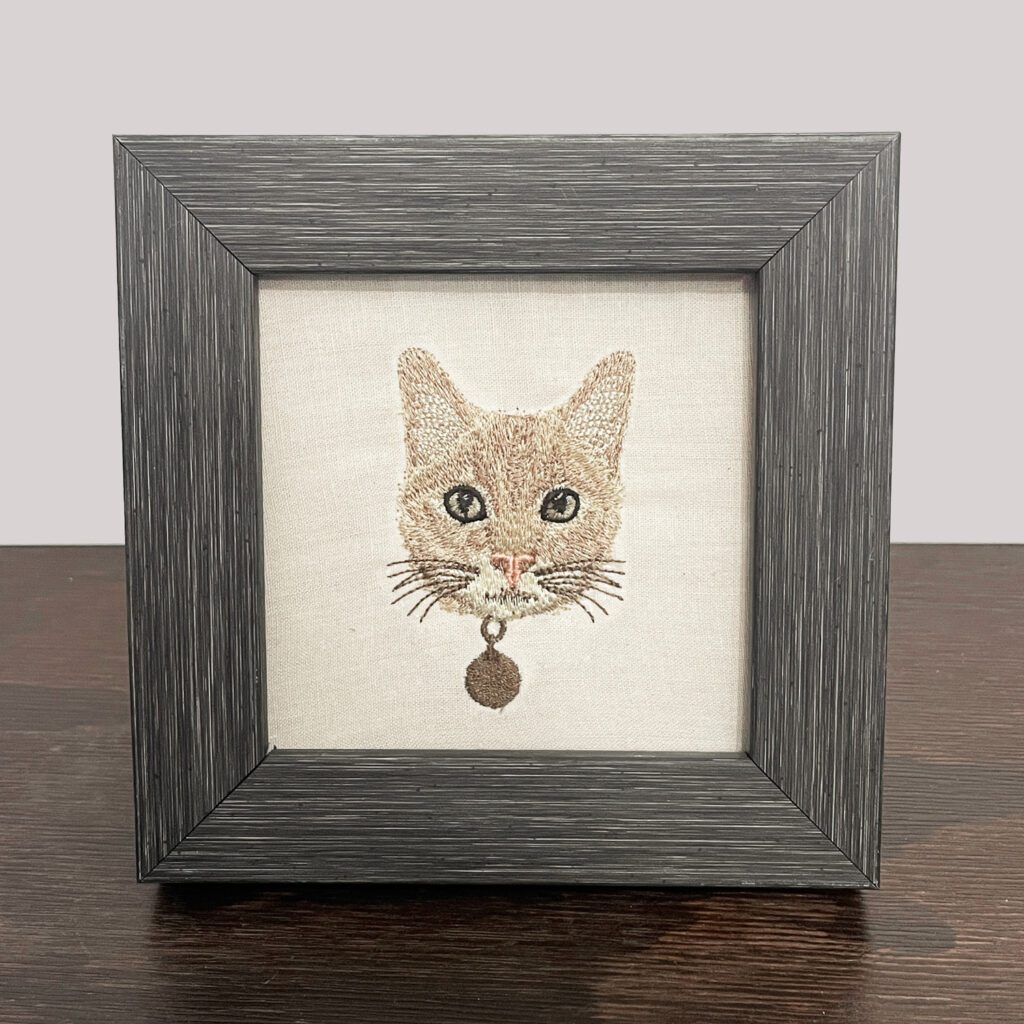 Framed machine embroidery design of a detailed cat pet portrait, showcasing fine stitching and vibrant thread colors, capturing the cat's unique features.