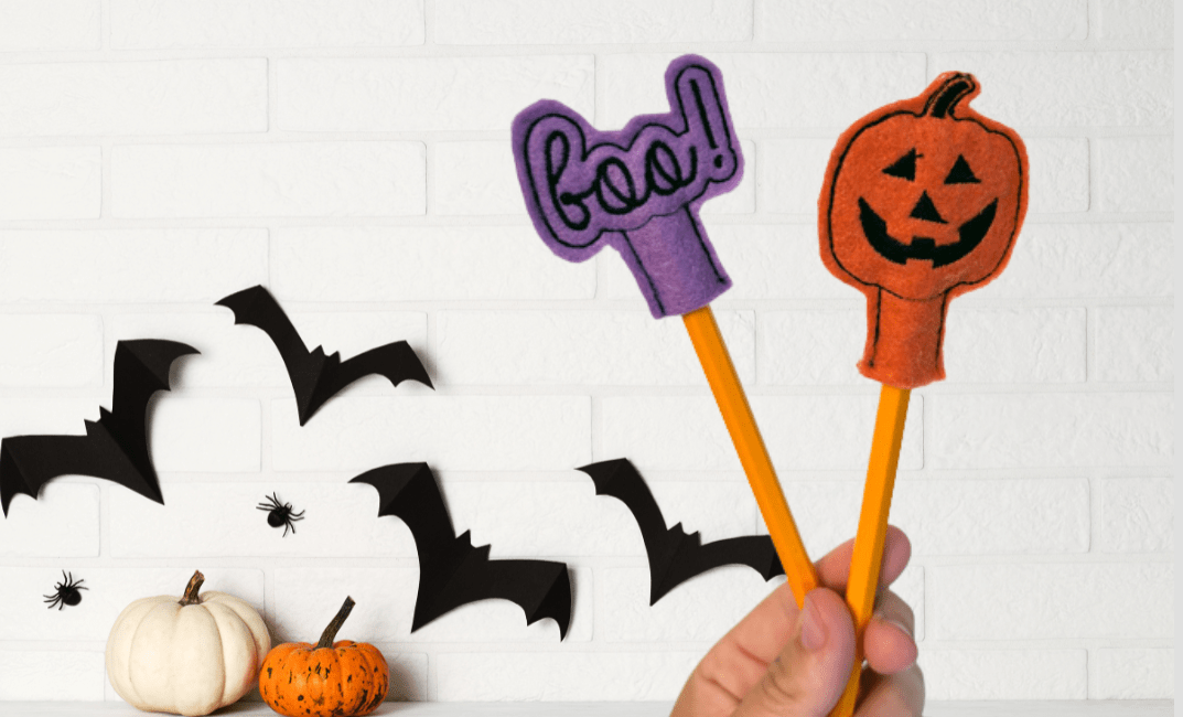 Person holding two Halloween embroidery pencil covers made with felt and thread – featuring a pumpkin and 'BOO' design.